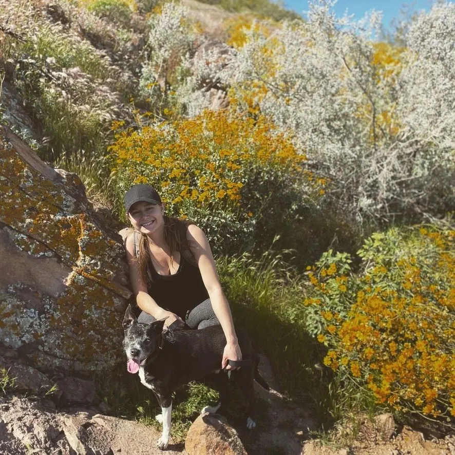 Molly sitting on a rocky hillside among yellow wildflowers with her dog