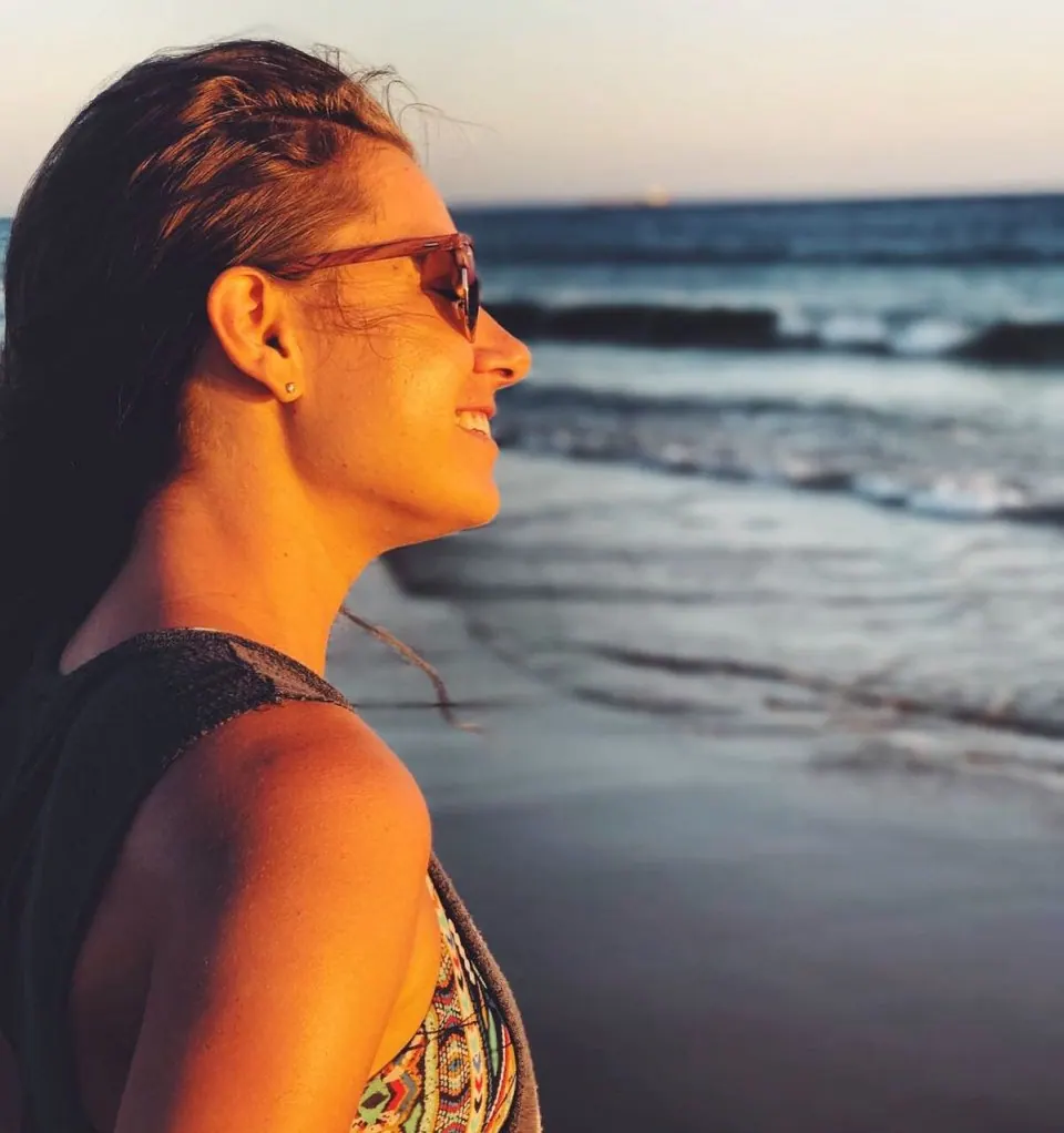 Molly in sunglasses smiling at the ocean in warm evening light