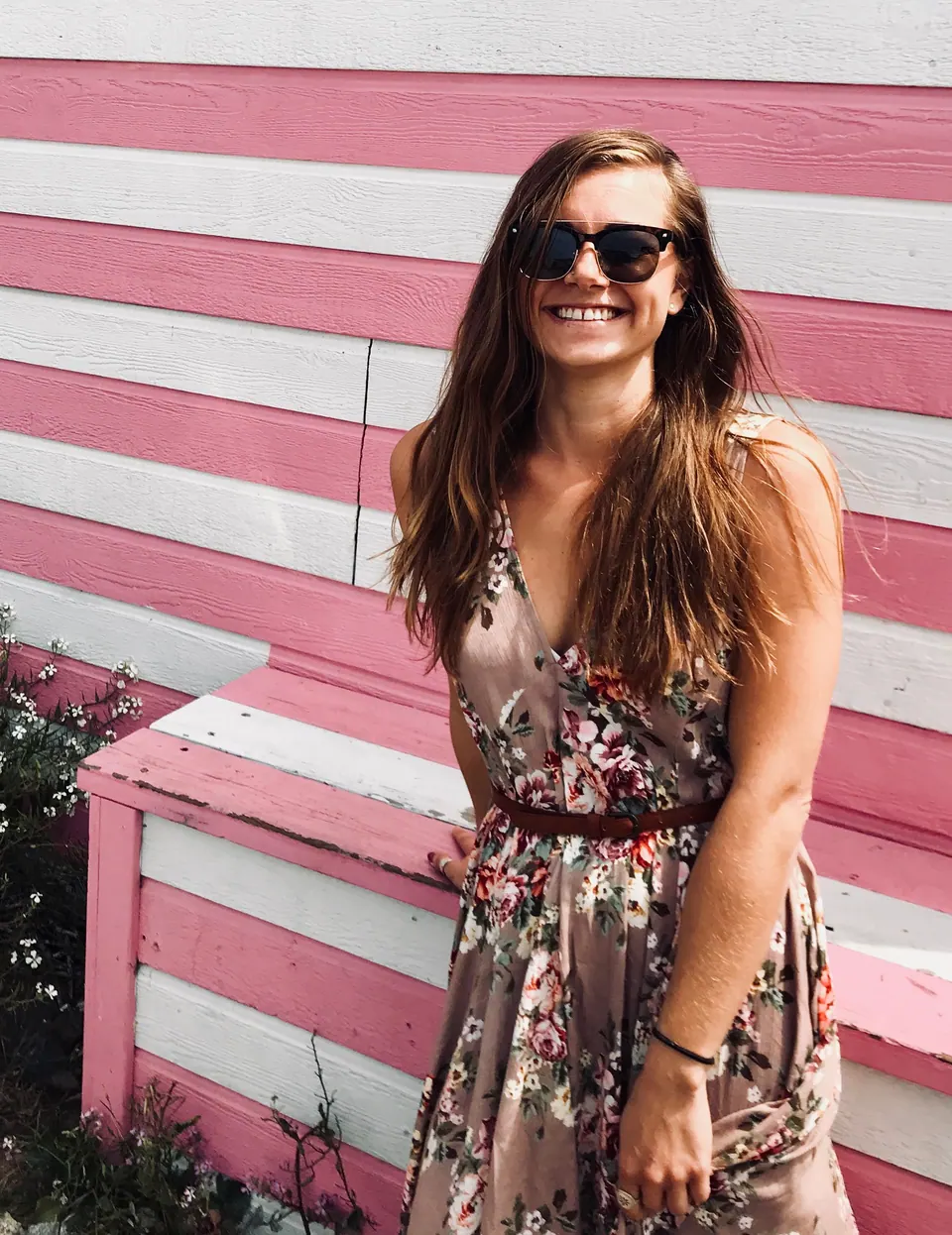 Molly laughing in a floral dress in front of a pink and white striped wall