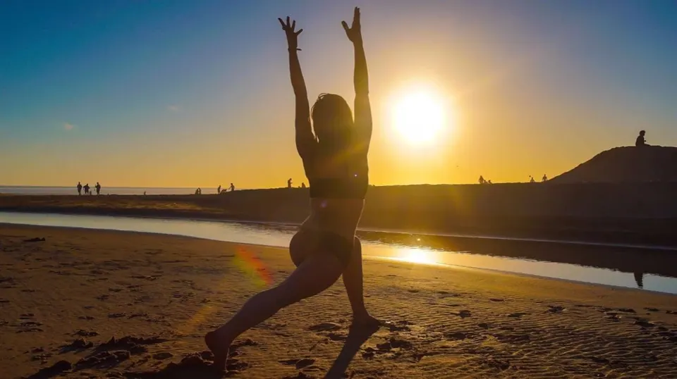 Molly in a yoga pose on a beach, silhouetted against the setting sun