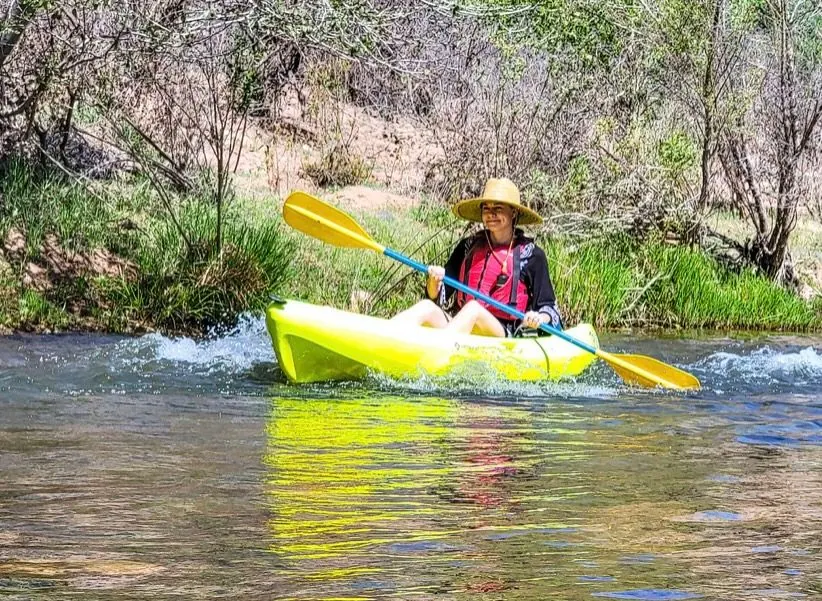 Molly paddling a bright yellow kayak down a small river