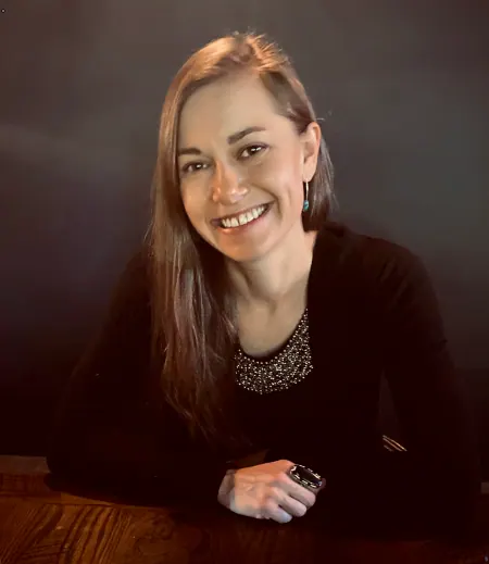 Portrait of Molly Borsom, smiling, seated at a wooden table