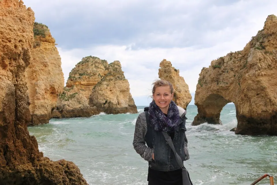 Molly standing in front of golden sea stacks and arches on a rocky coast