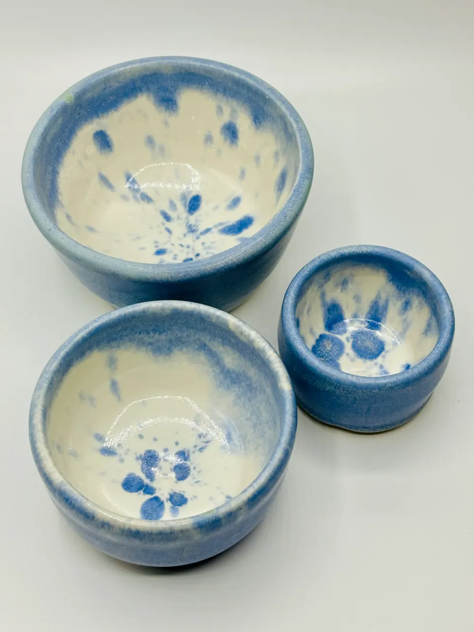 Three ceramic bowls in graduated sizes, glazed matte sky blue with white interiors speckled in blue