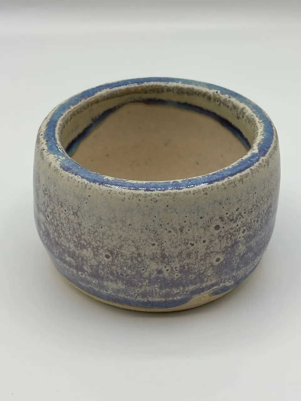 Small straight-sided ceramic bowl in a speckled lavender glaze with a blue rim and a bare clay interior