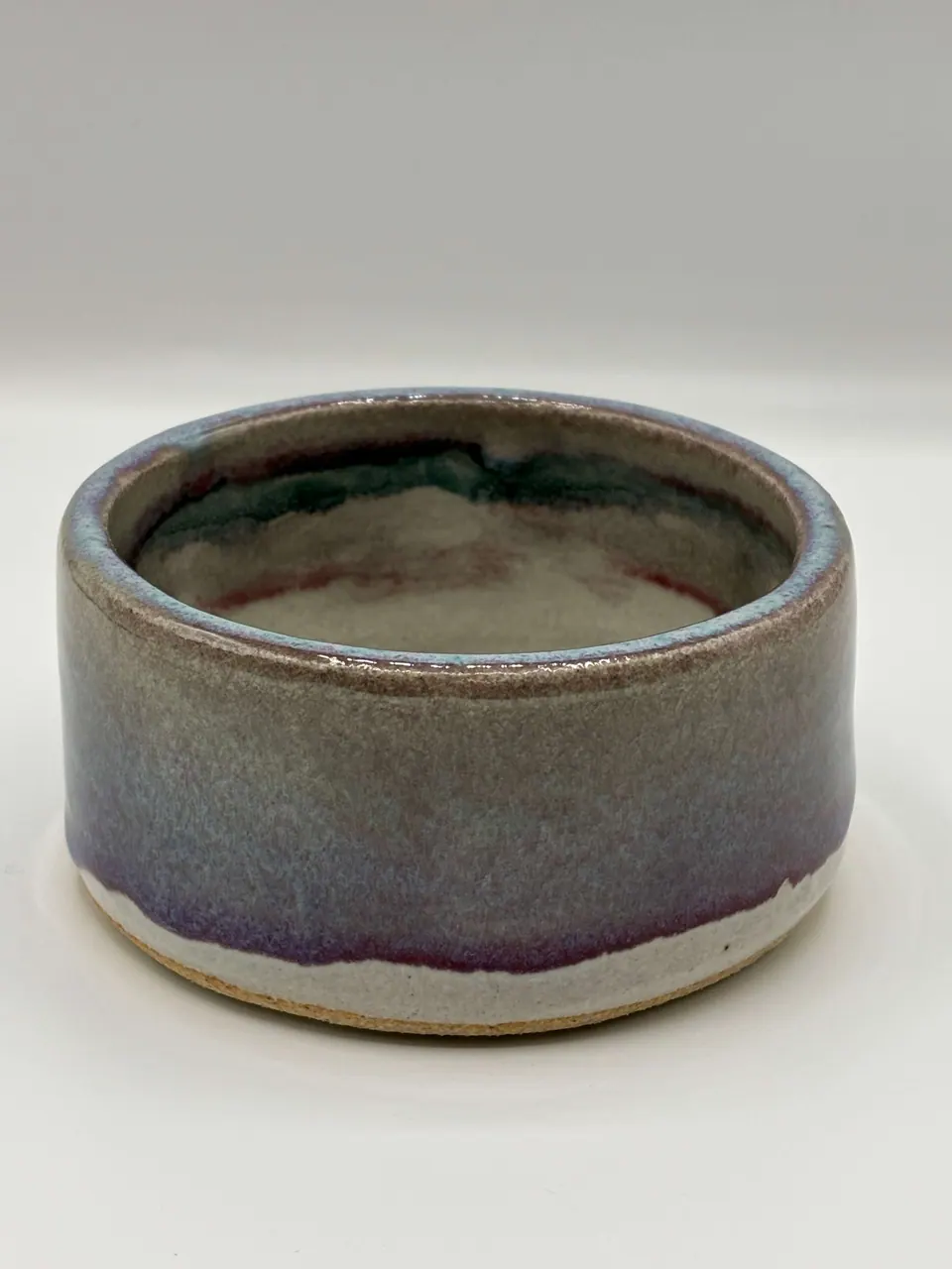 Low cylindrical ceramic dish with a glaze that shifts from grey-green to violet above a bare clay foot