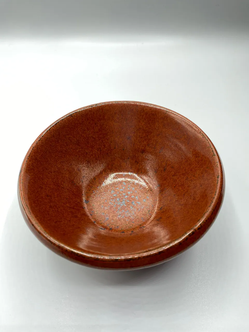 Deep ceramic bowl with a glossy rust-red glaze and a pale speckled center
