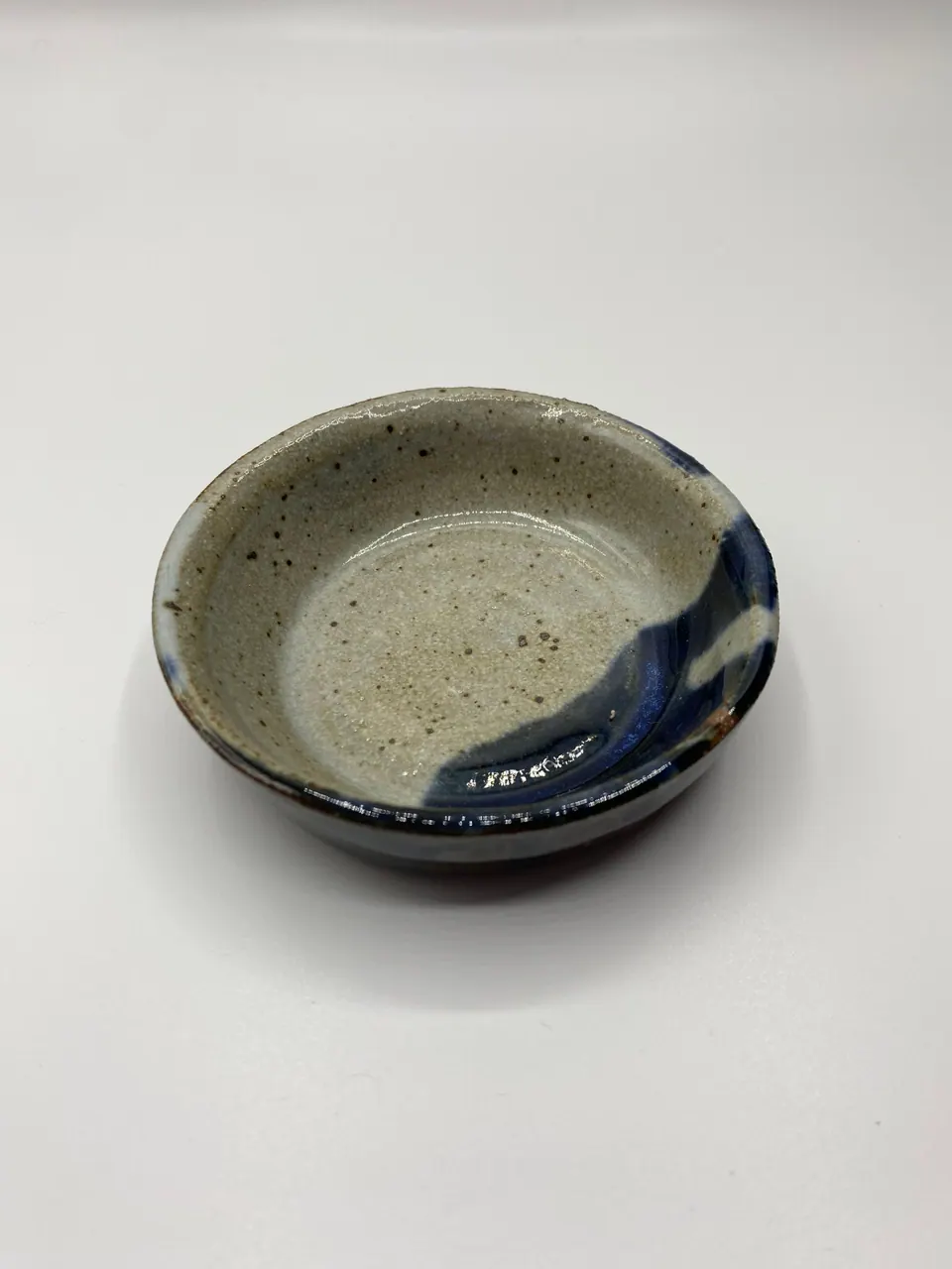 Shallow speckled grey ceramic dish with a sweep of dark blue glaze across one side