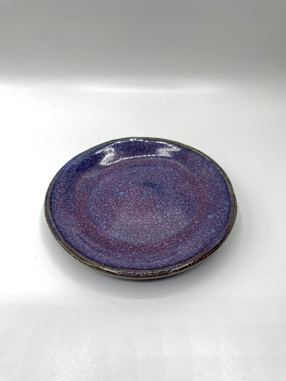 Small ceramic plate glazed in speckled violet with a blue rim