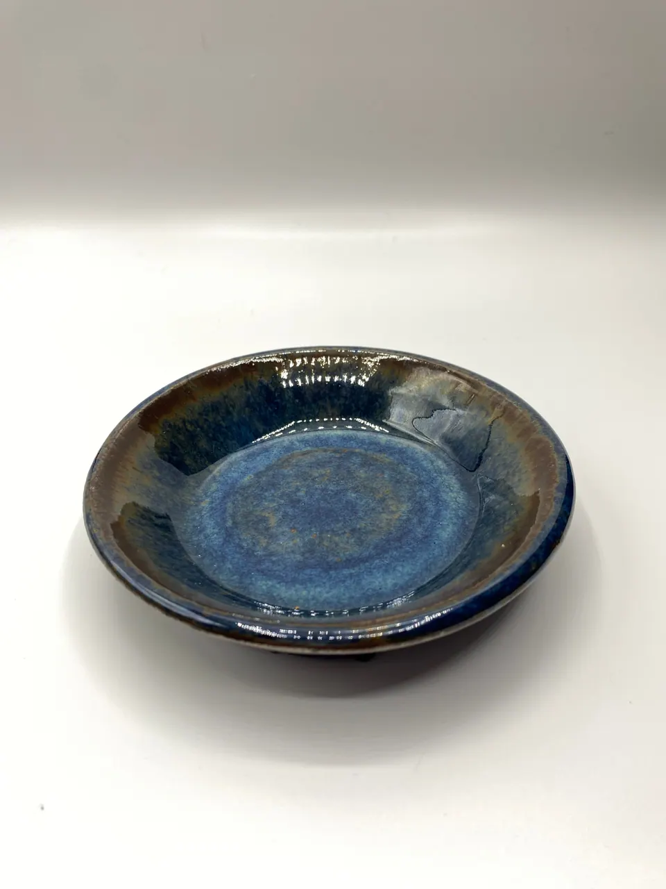 Shallow ceramic dish with a pooled bright blue glaze inside a dark rim