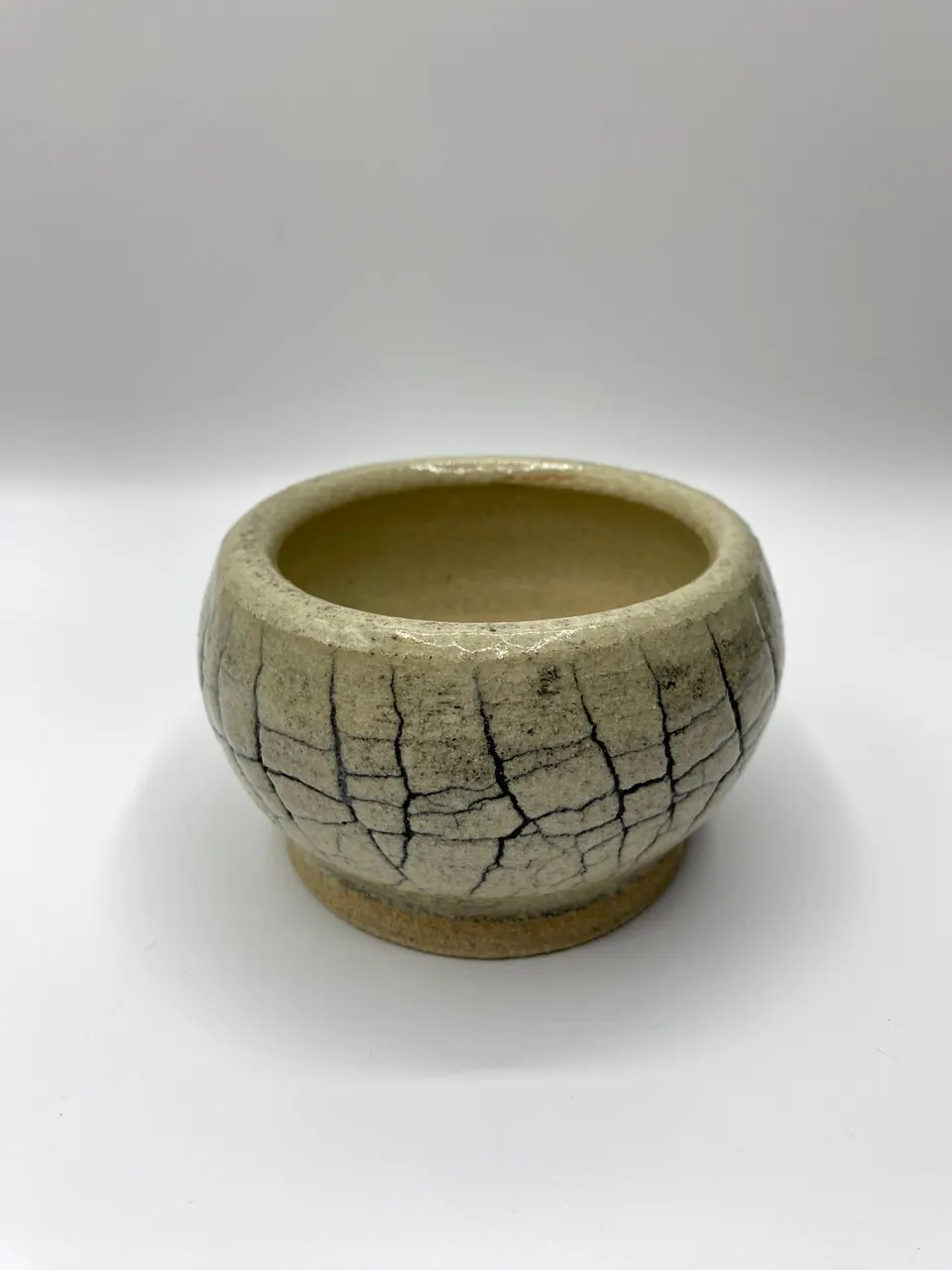 Round ceramic pot with a cream crackle glaze and dark fracture lines over a bare clay foot