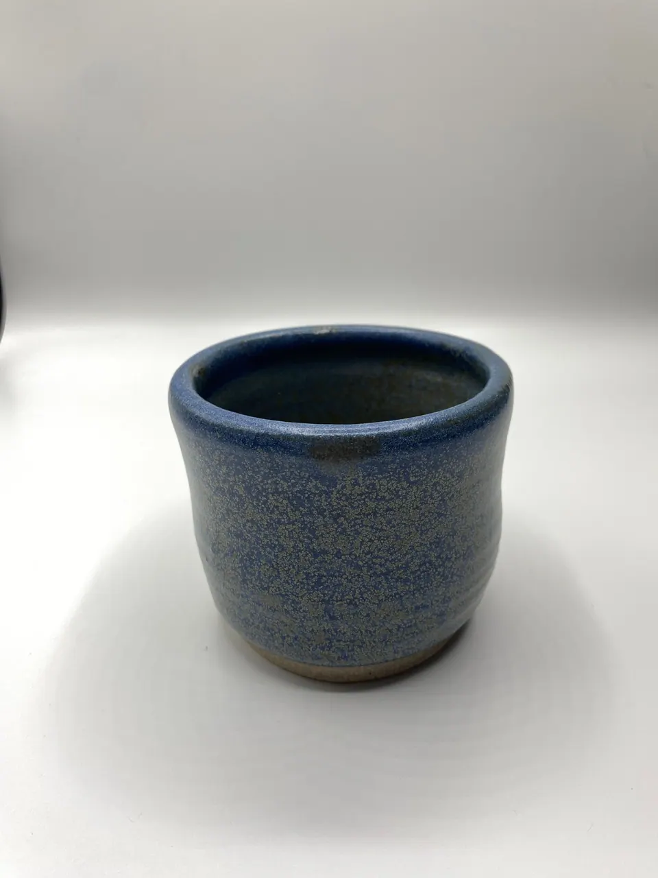 Handleless ceramic cup with a gently waisted body in a speckled denim blue glaze