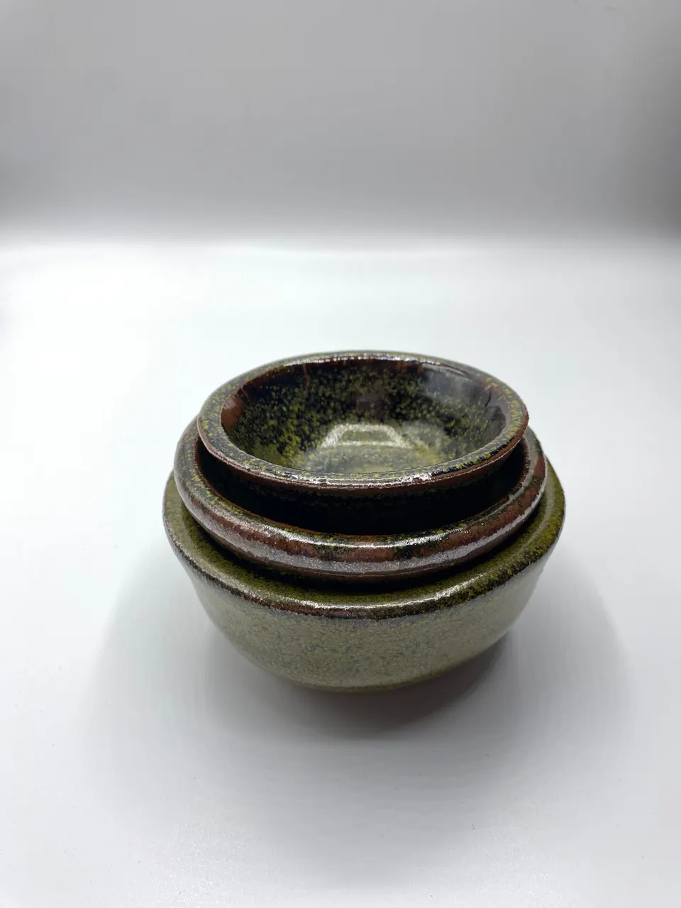 Four small ceramic bowls nested inside one another, glazed in mossy greens and browns