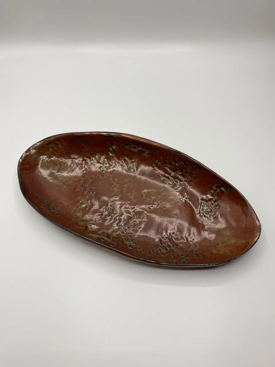 Hand-built oval ceramic tray in a glossy red-brown glaze with pale textured markings