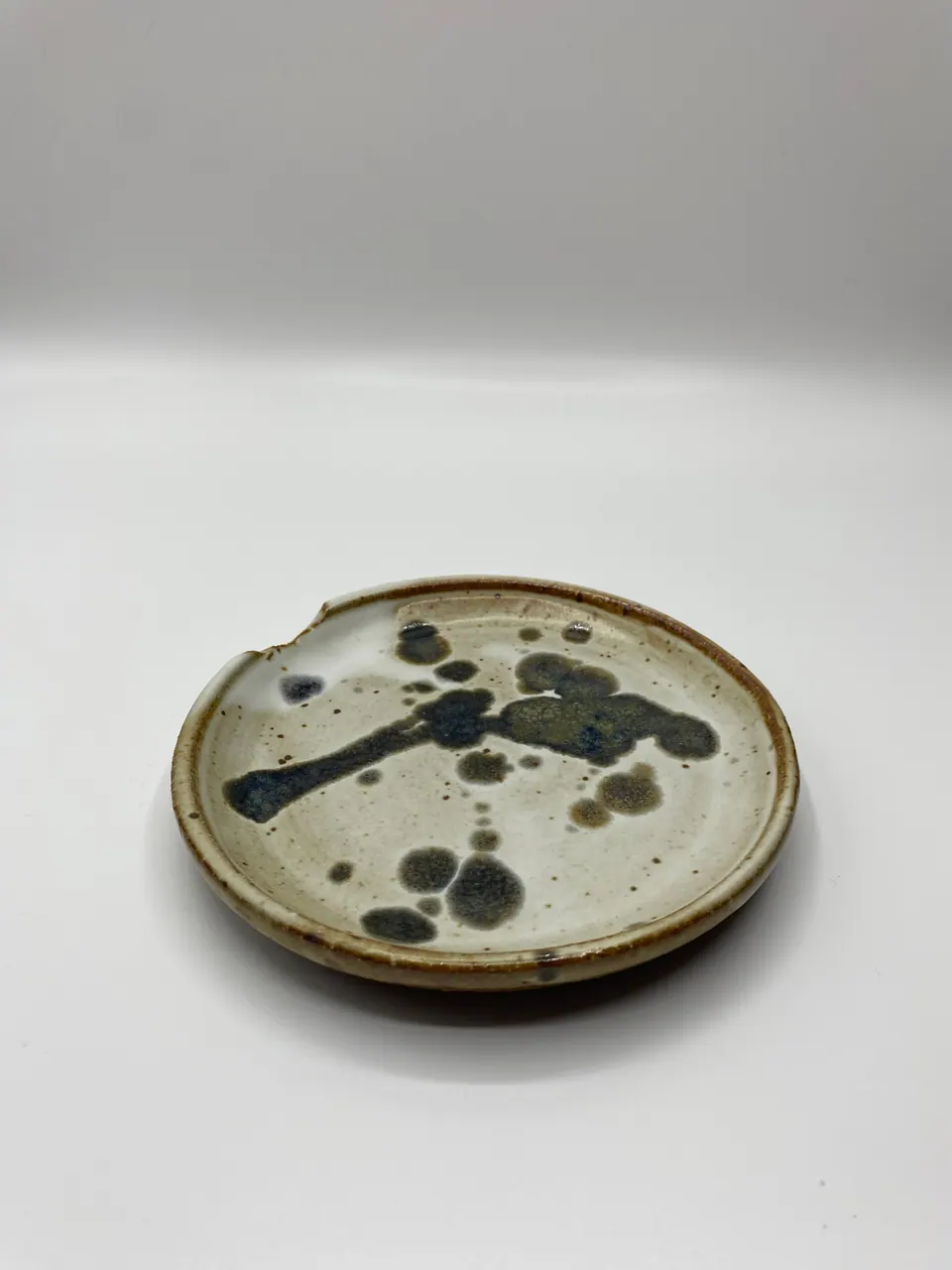 Small cream ceramic plate with black ink-like glaze splashes and a brown rim