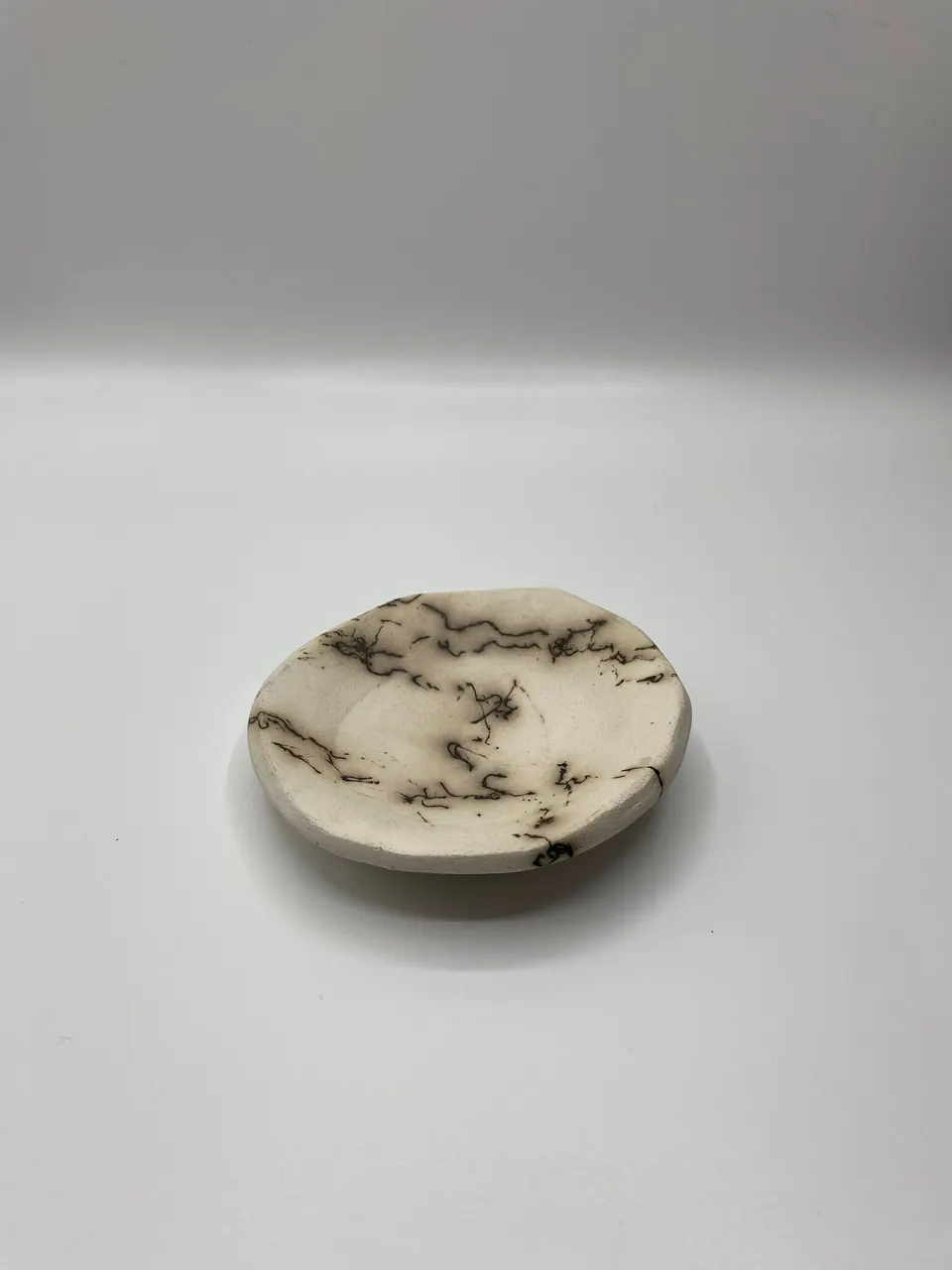 Small white ceramic dish marked with fine black feathery carbon lines