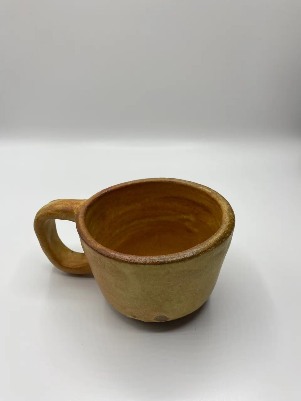 Hand-built ceramic mug with a looped handle in a warm ochre glaze