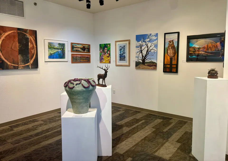Gallery corner with colorful paintings on the walls and a large green ceramic vessel, a bronze elk and other sculptures on white plinths