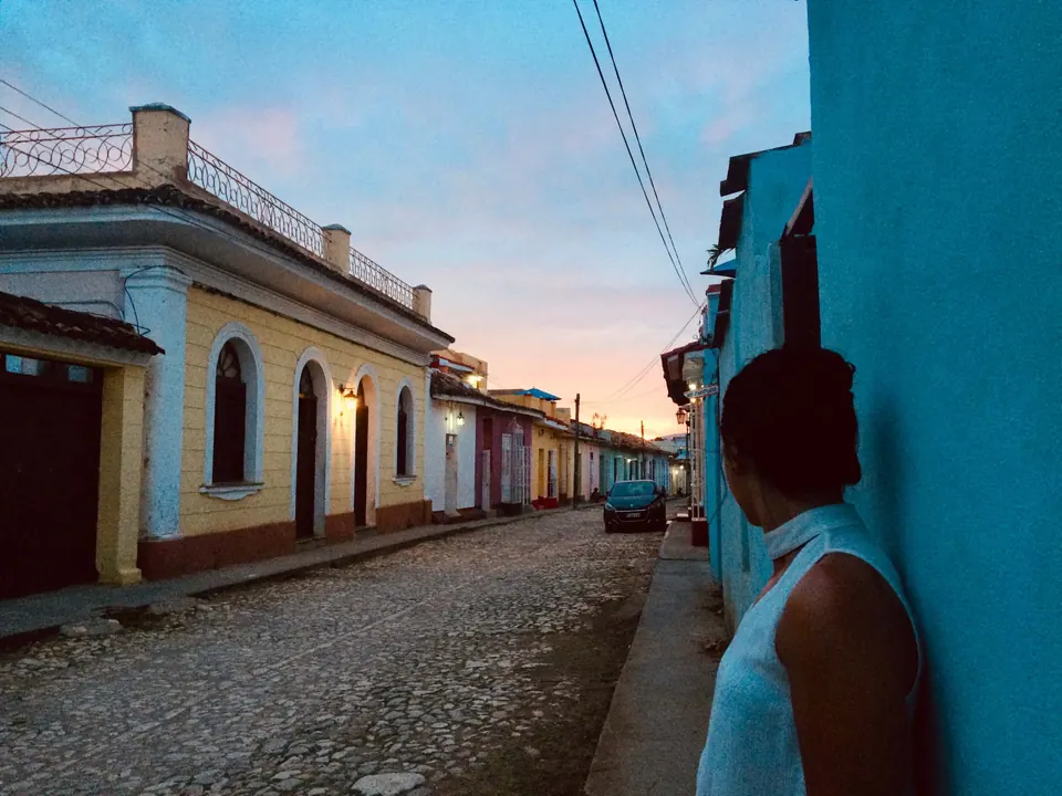 Person leaning against a bright blue wall on a cobbled street of pastel colonial houses at dusk