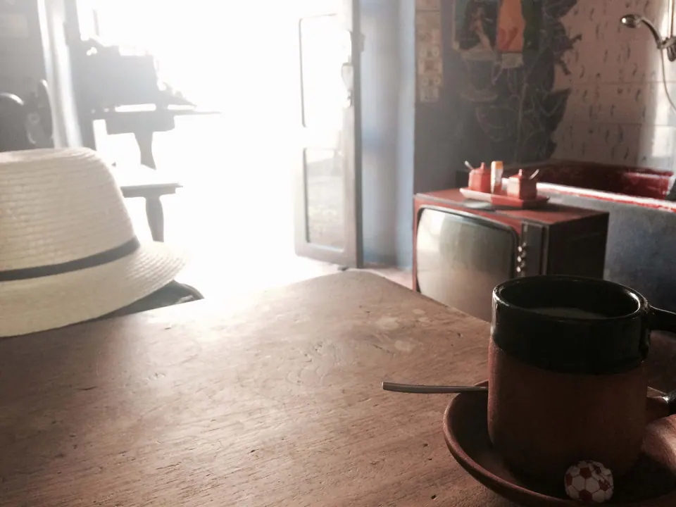 Sunlight flooding through an open doorway onto a wooden table with a straw hat and a coffee pot