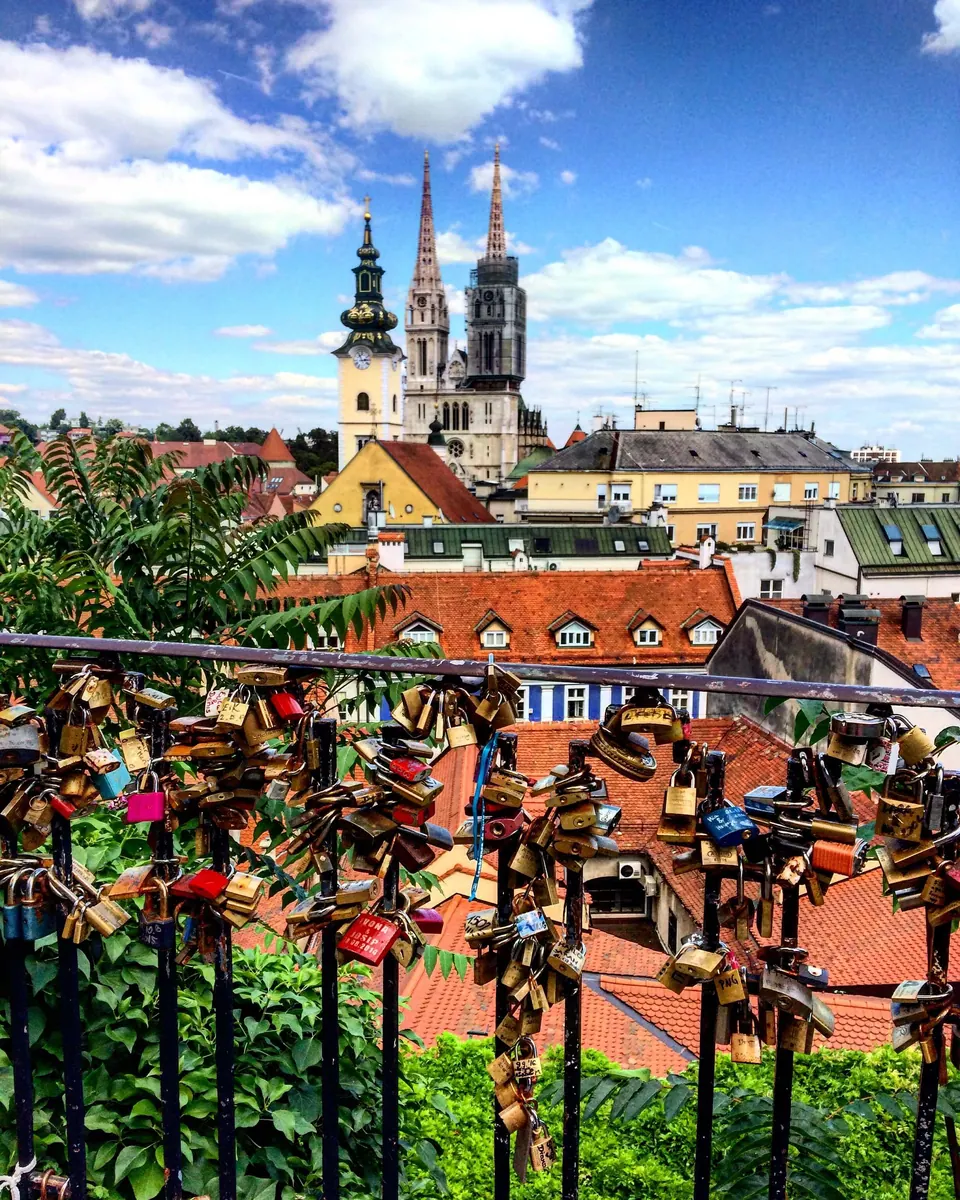 Railing covered in padlocks overlooking red rooftops and twin cathedral spires